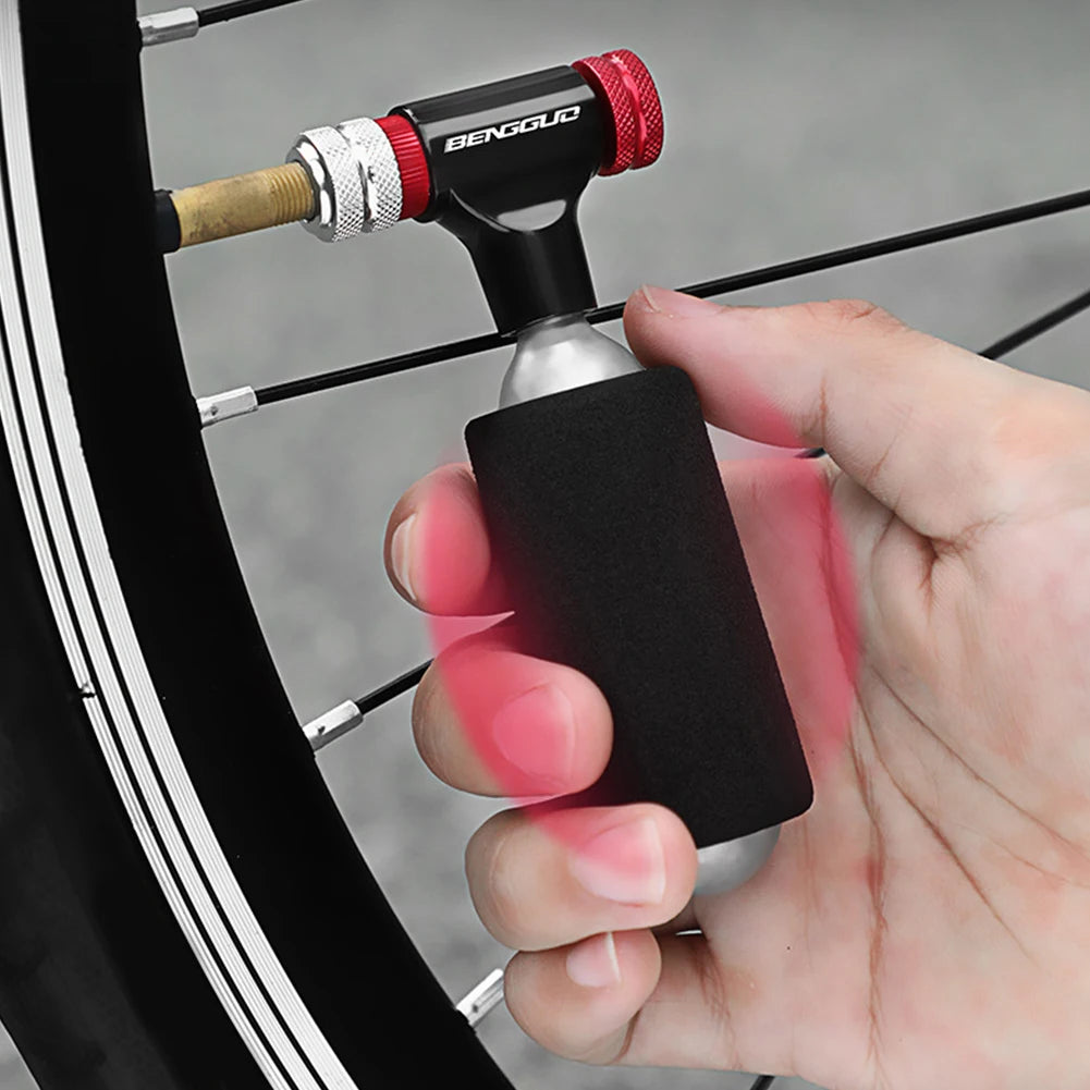 Hand holding a bicycle pump with a black and red handle, attached to a bicycle tire.