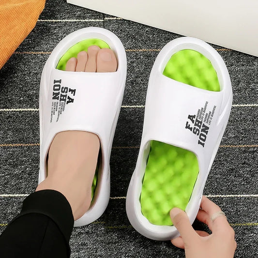 White slides with green sole worn by a person on a dark floor.