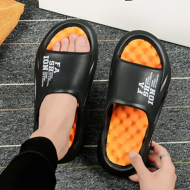 Black slides with orange soles worn by a person on a textured floor.
