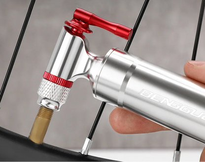 Bicycle air pump with interchangeable nozzles held by a hand, against a blurred background.