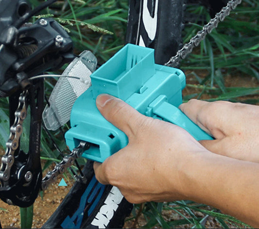 Person using a turquoise chain tool on a bicycle chain with grass in the background