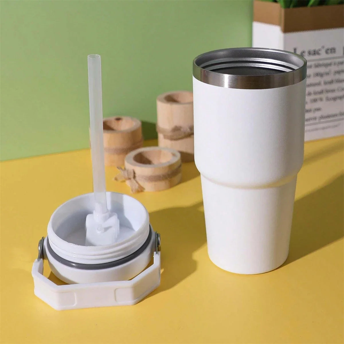White tumbler with straw and lid on a yellow surface with a green background