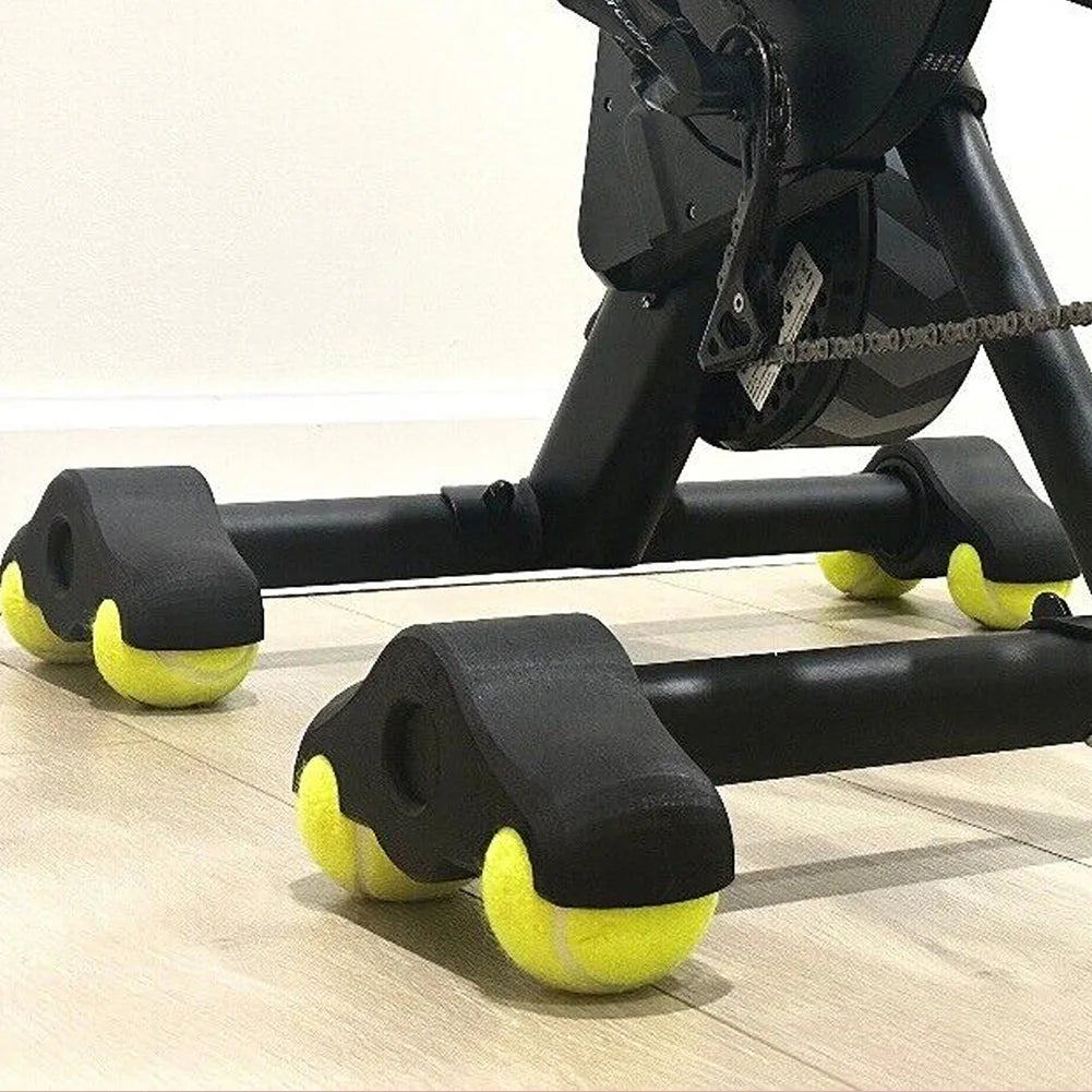 Exercise bike with tennis balls attached to the wheels on a wooden floor.
