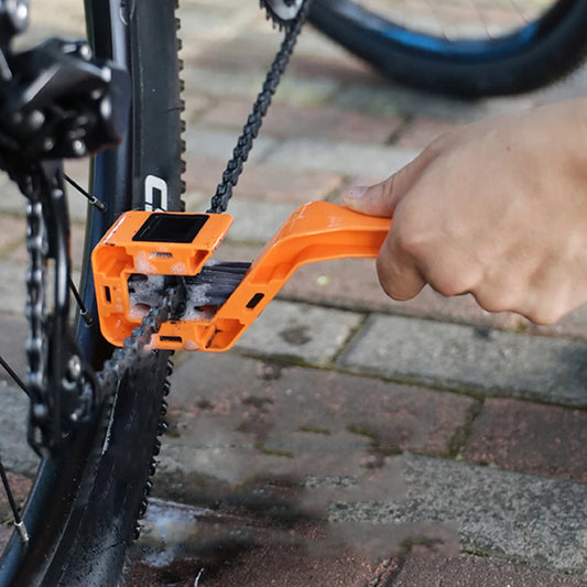 Person using an orange bicycle chain scrubber tool on a bike chain outdoors.