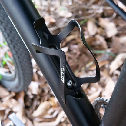 Black bicycle water bottle holder attached to a bike frame with a blurred natural background