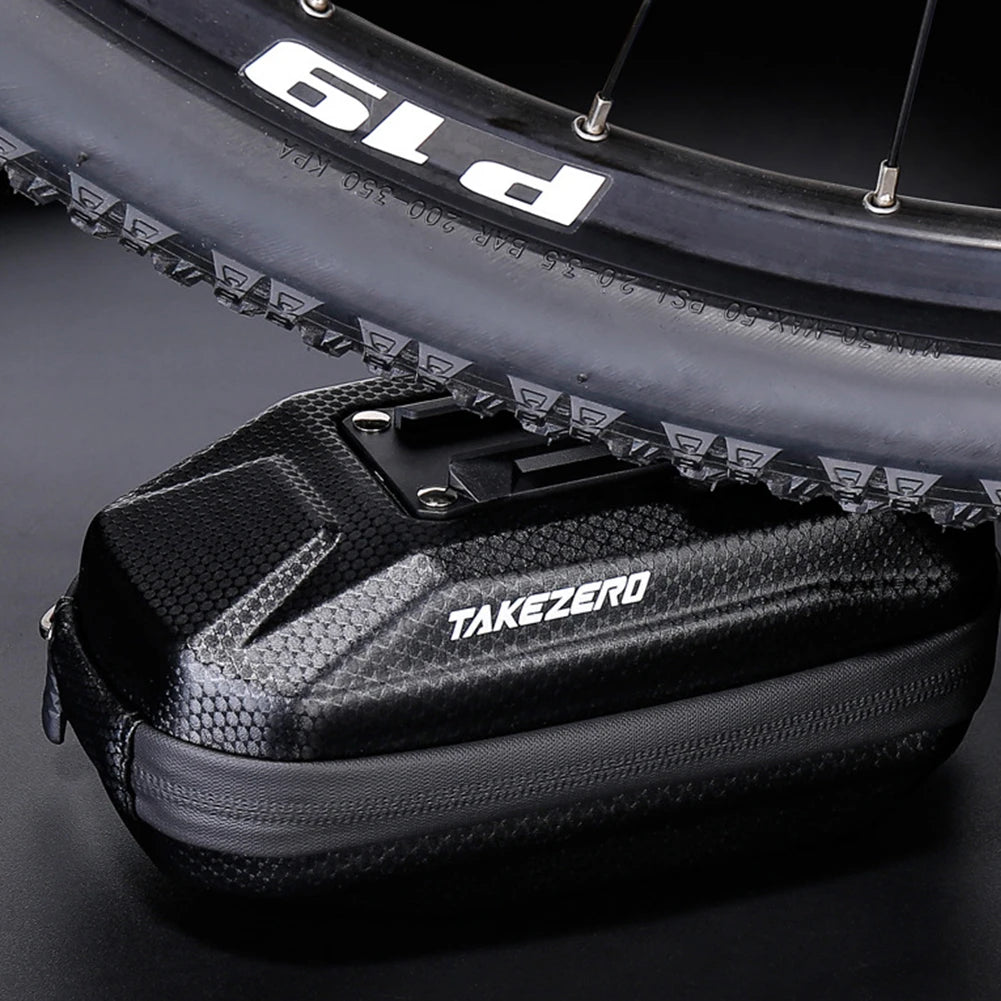 Black cycling bag with 'TAKEZERO' branding in front of a bicycle wheel.