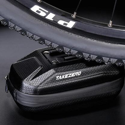 Black cycling bag with 'TAKEZERO' branding in front of a bicycle wheel.